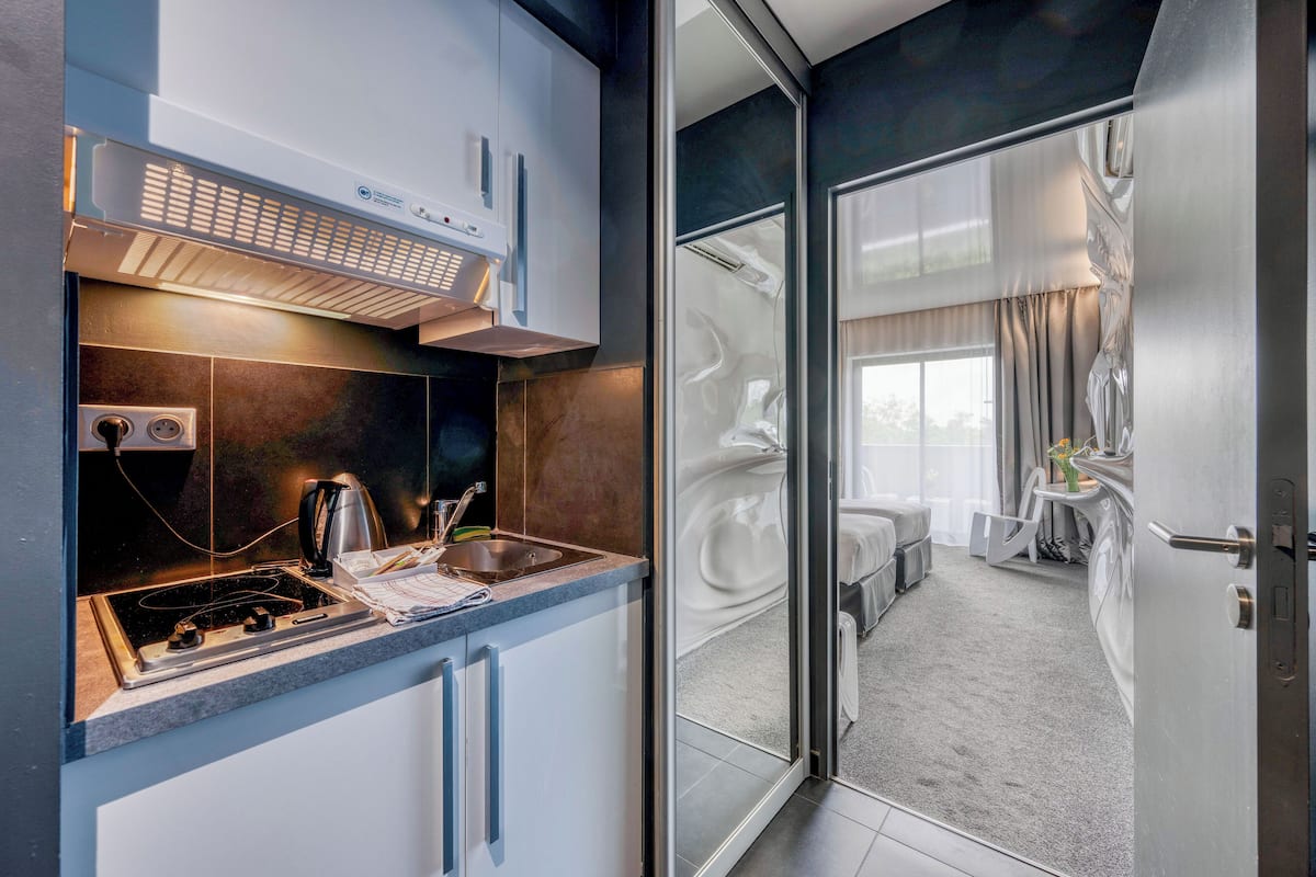 Une cuisine moderne dotée d’une cuisinière intégrée et d’une machine à café, ainsi qu’une porte vitrée donnant sur une chambre à coucher avec un lit et une petite table.