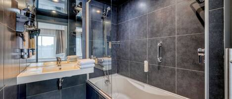 A modern bathroom with a large bathtub, a glass-enclosed shower, and a vanity with a mirror and towel rack.