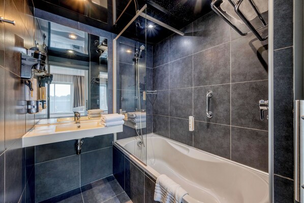 Un baño moderno con una bañera grande, una ducha con cerramiento de vidrio y un tocador con espejo y toallero.