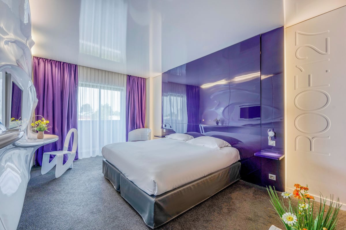 Une chambre d’hôtel moderne dotée d’un grand lit, d’une coiffeuse avec un miroir et d’un coin salon avec un fauteuil.