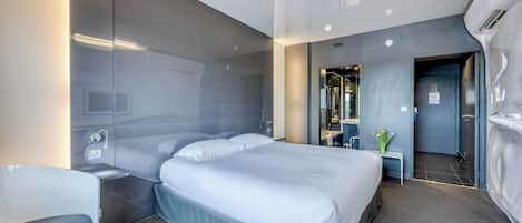 Una habitación de hotel moderna con una cama grande, mesitas de noche, un pequeño rincón de descanso y un baño visible a través de una puerta abierta.