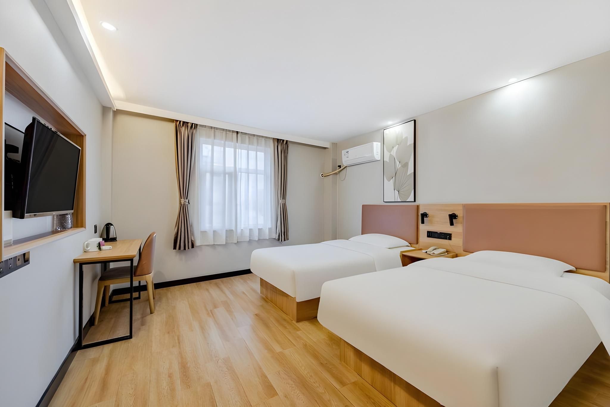 Una habitación de hotel con cama, escritorio con silla, televisor y ventana con cortinas.