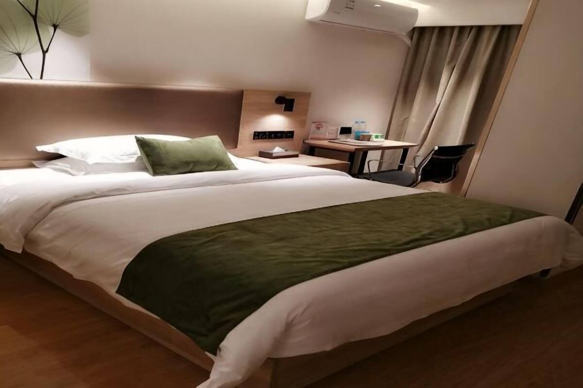 A hotel room with a large bed, a bedside table with a lamp, a chair, and a desk with a computer.