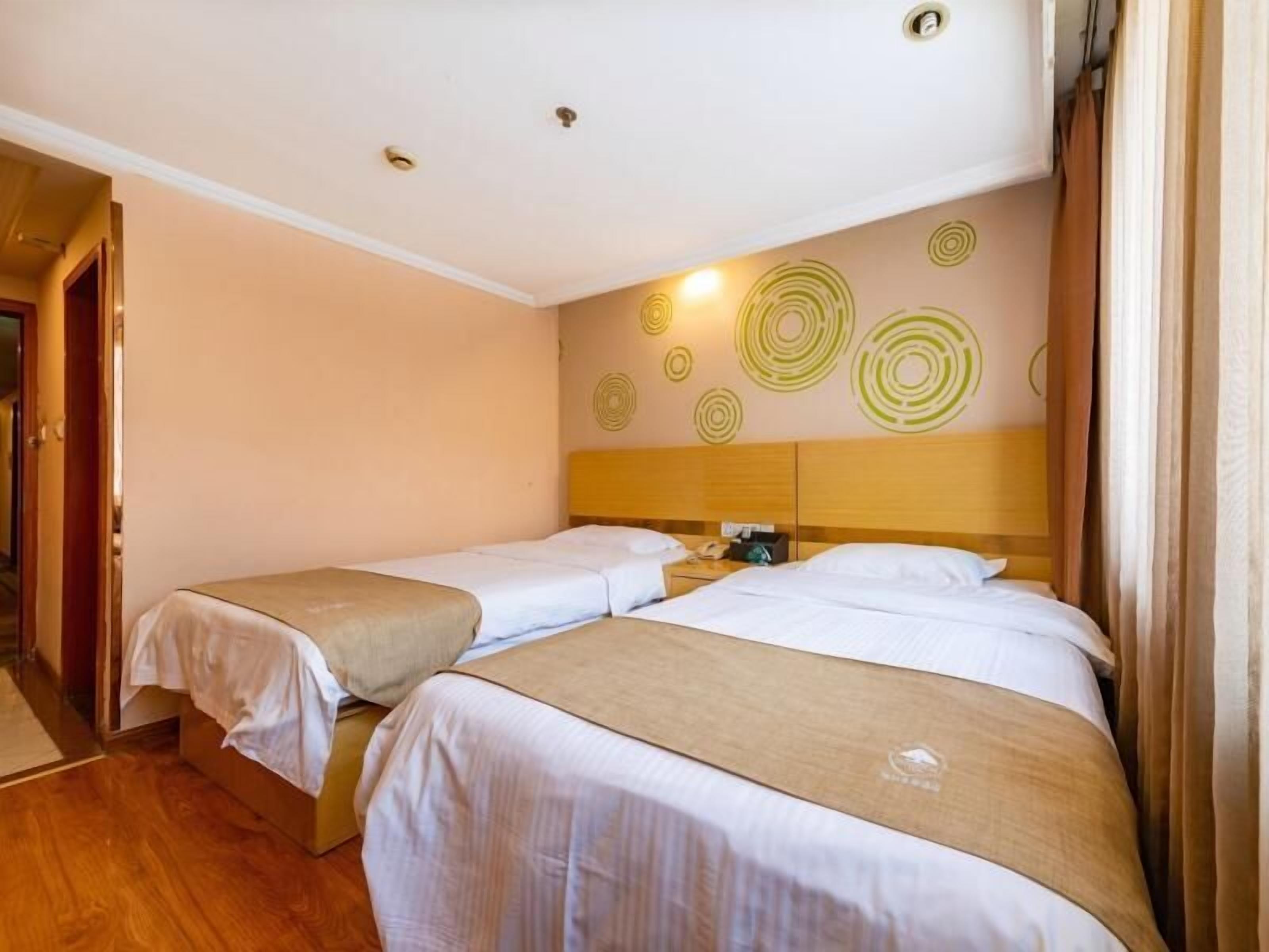 A hotel room with two single beds, a wooden headboard, a wall with circular patterns, and a door to the left.