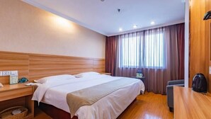 A hotel room with a wooden headboard, a large bed, a desk with a chair, a window with curtains, and a kettle on the desk. - Greentree Inn Yancheng Dafeng Hotel (Yancheng)