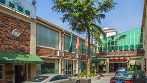 A hotel with a brick facade, large windows, and a green awning. There are cars parked in front and a tree in the center. - GreenTree Inn Shanghai Chongming Bao Town Express Hotel (Shanghai)
