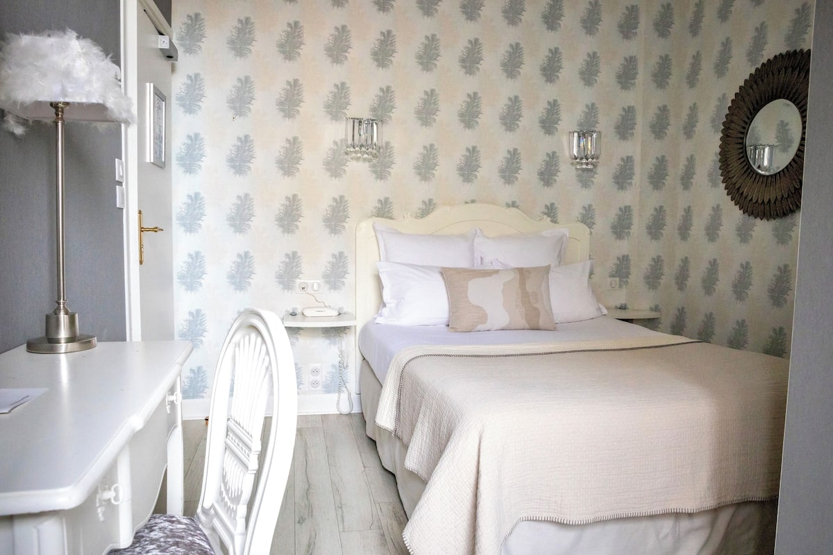 A bedroom with a bed, a bedside table, a lamp, and a wall with a leaf pattern.