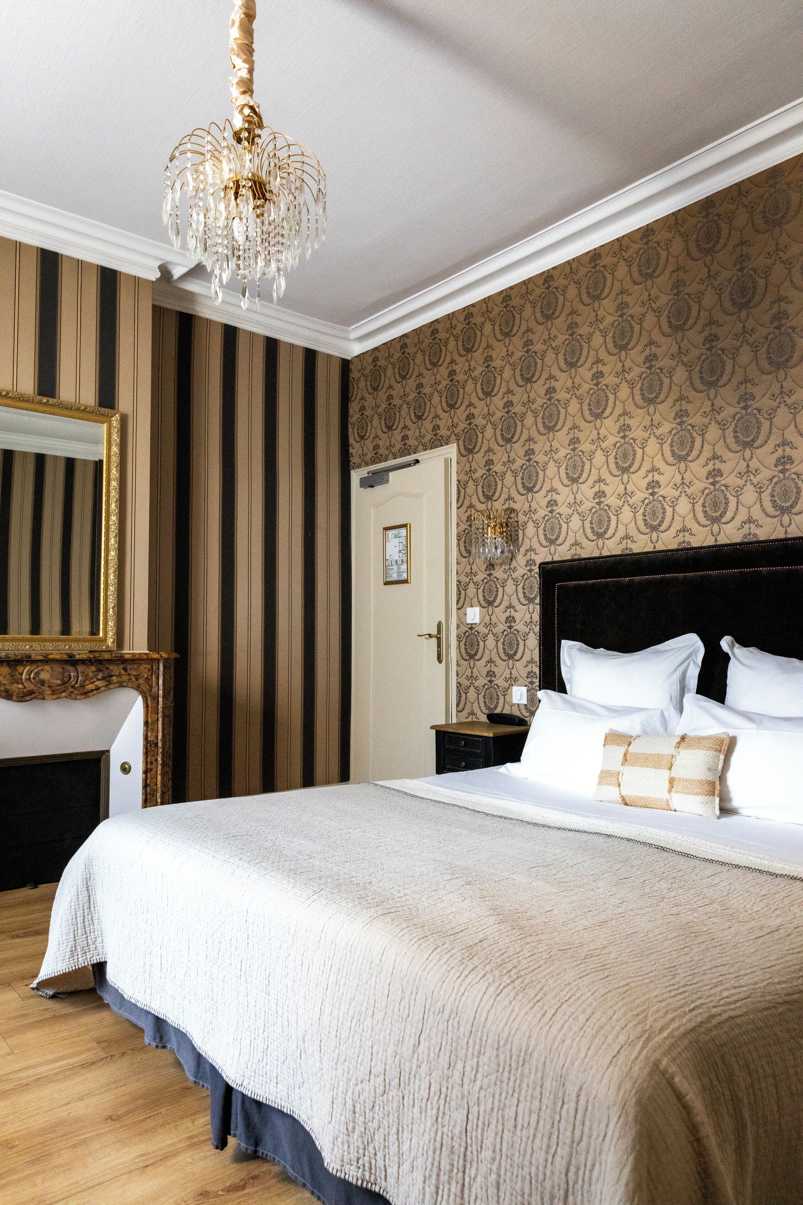Una habitación de hotel con una cama grande, un candelabro, un espejo y papel tapiz a rayas.