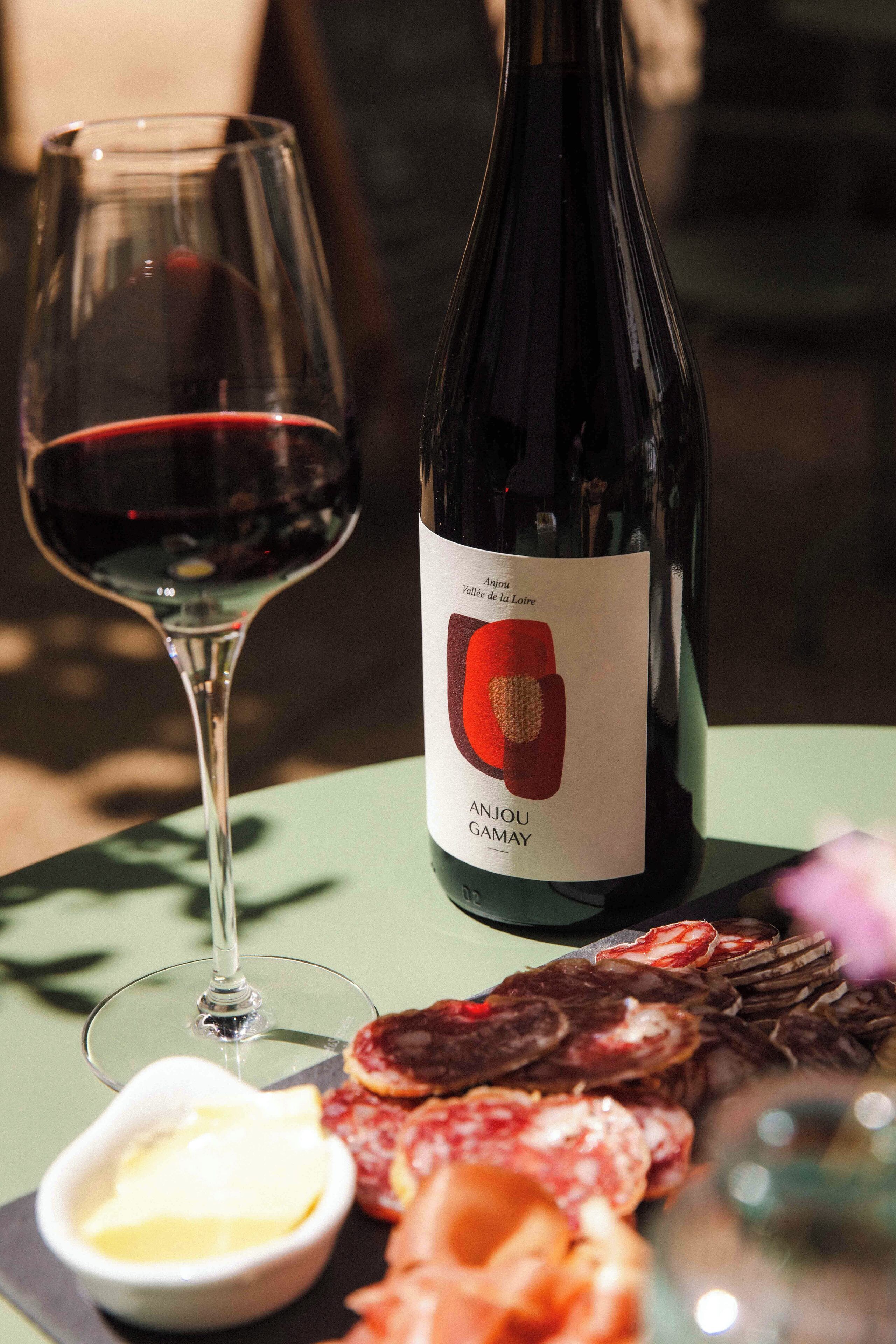 A bottle of wine, a glass of red wine, and a charcuterie board with various meats and a small bowl of butter on a table.