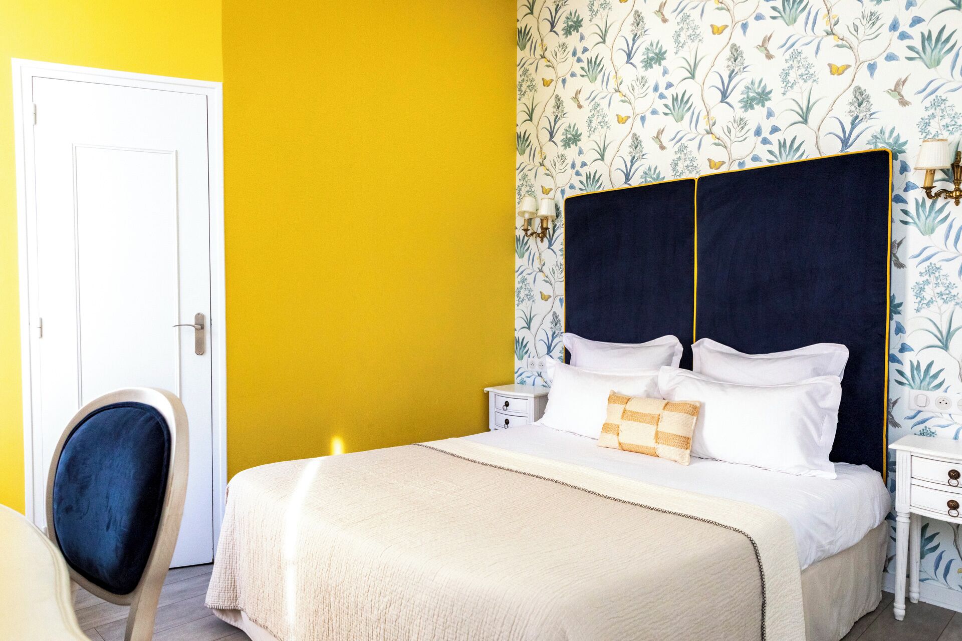 Un dormitorio con cama, una silla, una mesita de noche y un papel tapiz floral.