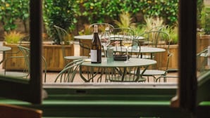 Un espace de restauration en plein air avec des tables et des chaises, une bouteille de vin et un verre de vin posés sur l’une des tables.