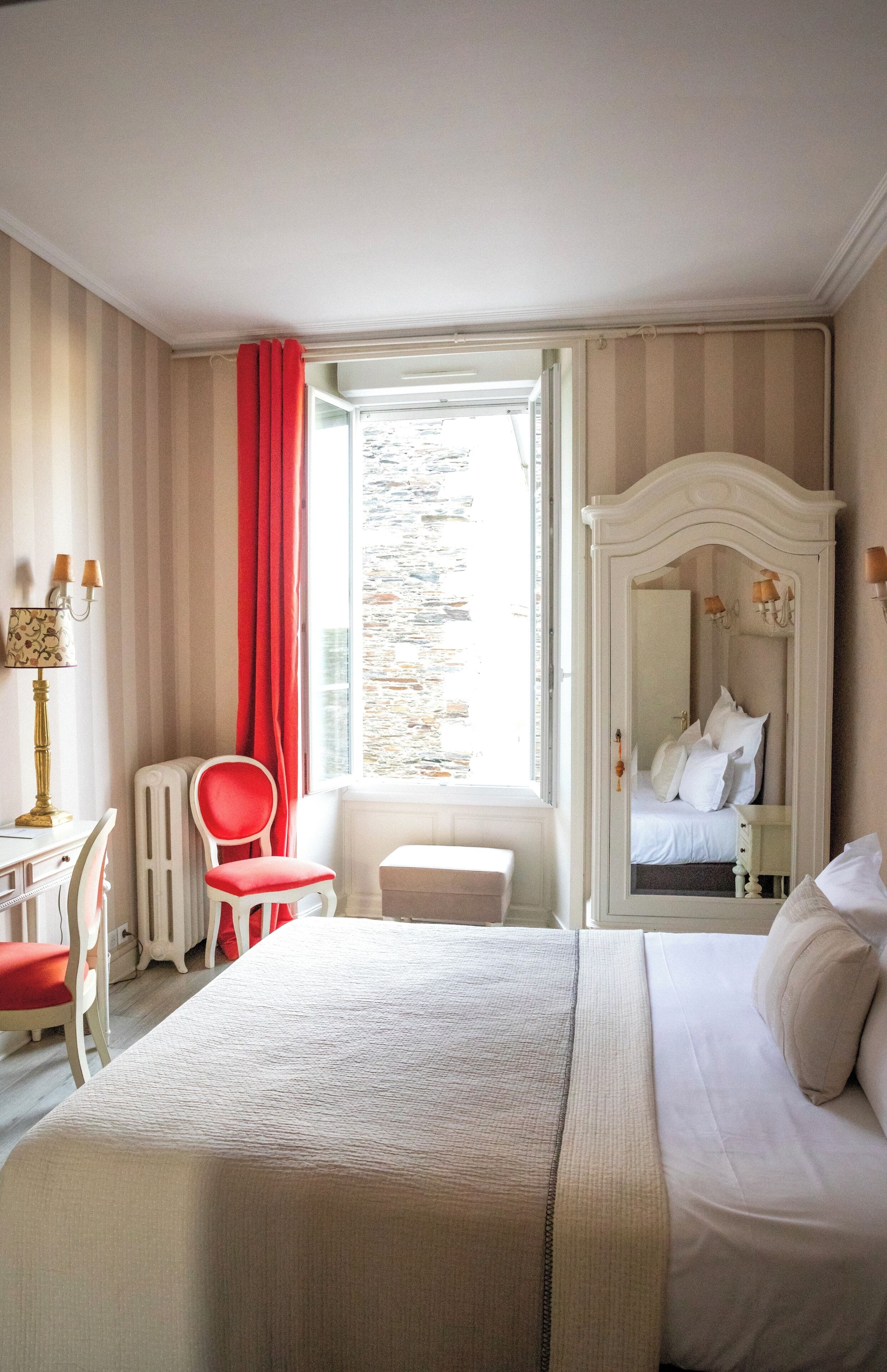 Hotelkamer met een bed, een bureau, een stoel, een dressoir en een raam met uitzicht op een stenen muur.