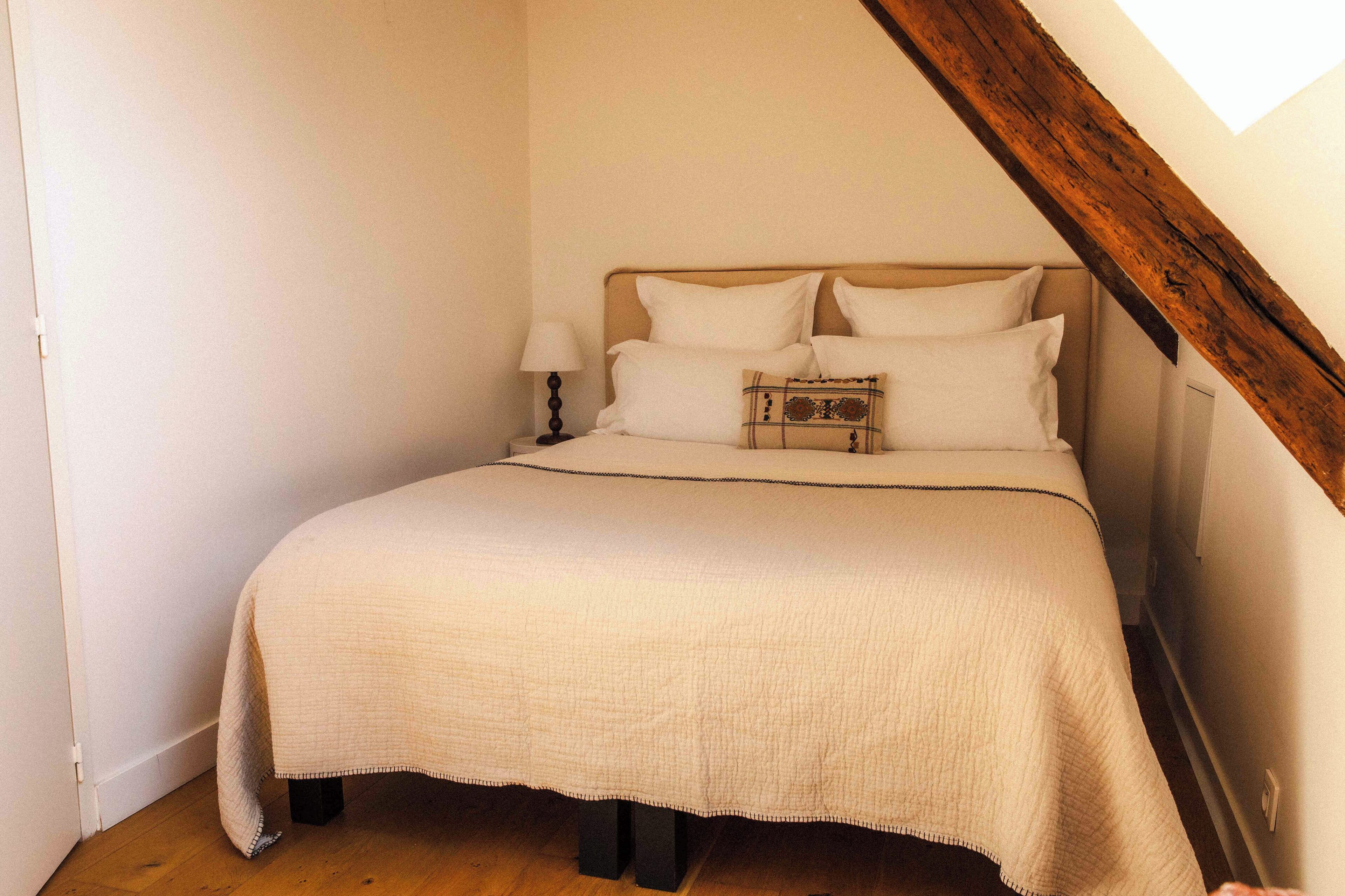 Une chambre à coucher avec un lit, des oreillers, une lampe de chevet et une structure en poutres apparentes.