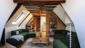 Un salon chaleureux aménagé dans les combles, avec des canapés verts, une table basse en bois et des poutres apparentes.