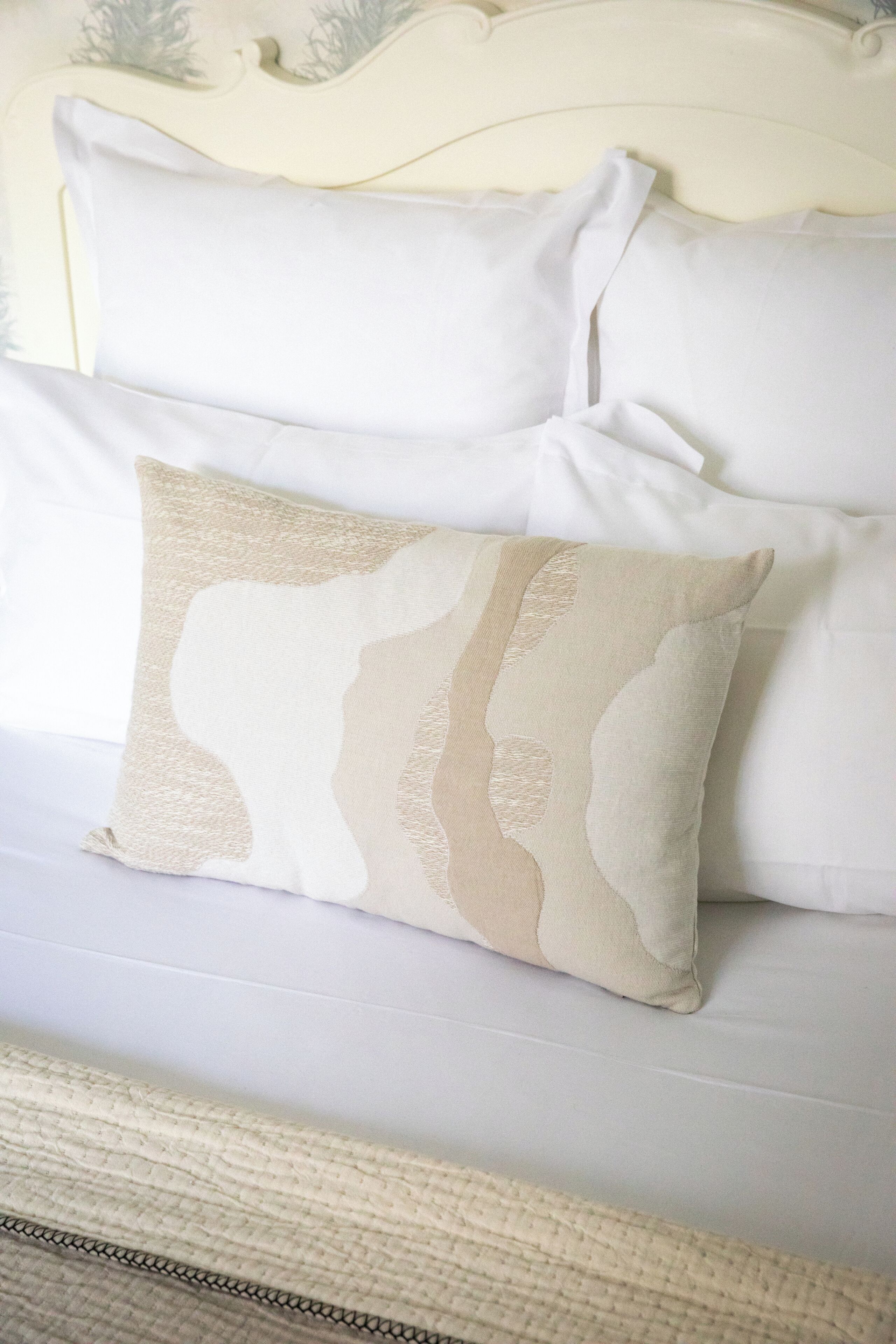 A bed with white bedding and a decorative beige pillow with a silhouette design.