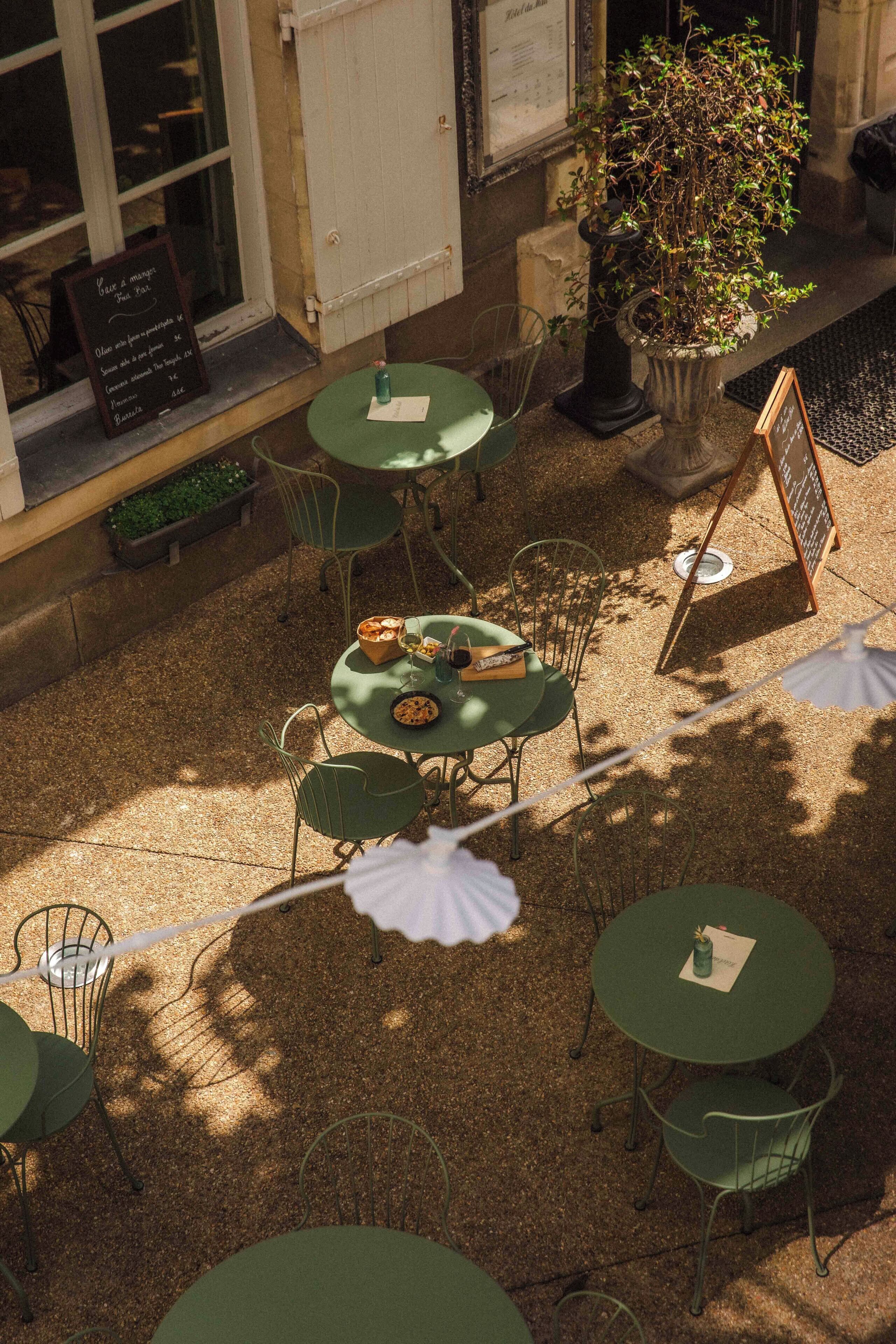 Un café al aire libre con mesas y sillas redondas, una planta en maceta y un menú en la pizarra.