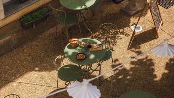 Un café al aire libre con mesas y sillas redondas, una planta en maceta y un menú en la pizarra.