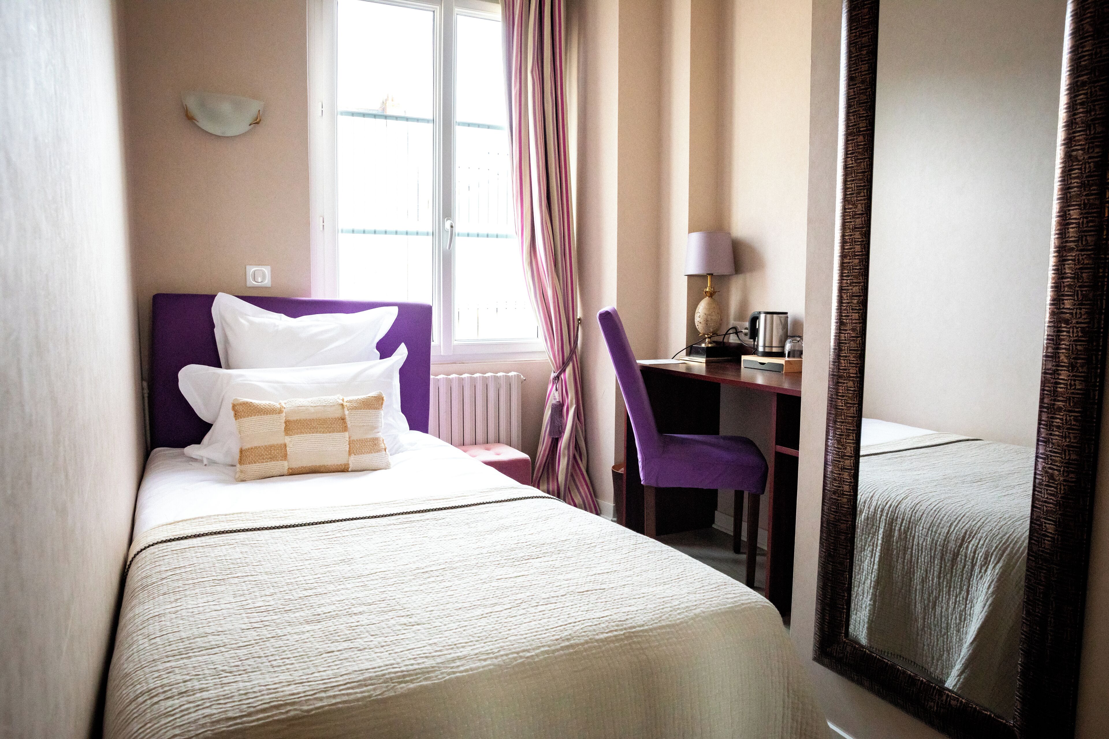 Habitación de hotel con cama, escritorio, silla, ventana y espejo.