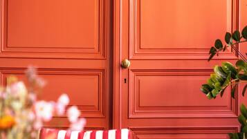 Una habitación con una puerta roja, un cojín a rayas en una silla y un florero con flores.