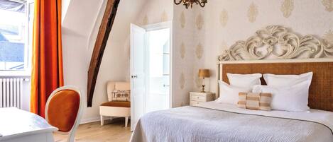 A bedroom with a large bed, a chandelier, a white headboard, and a window with orange curtains.