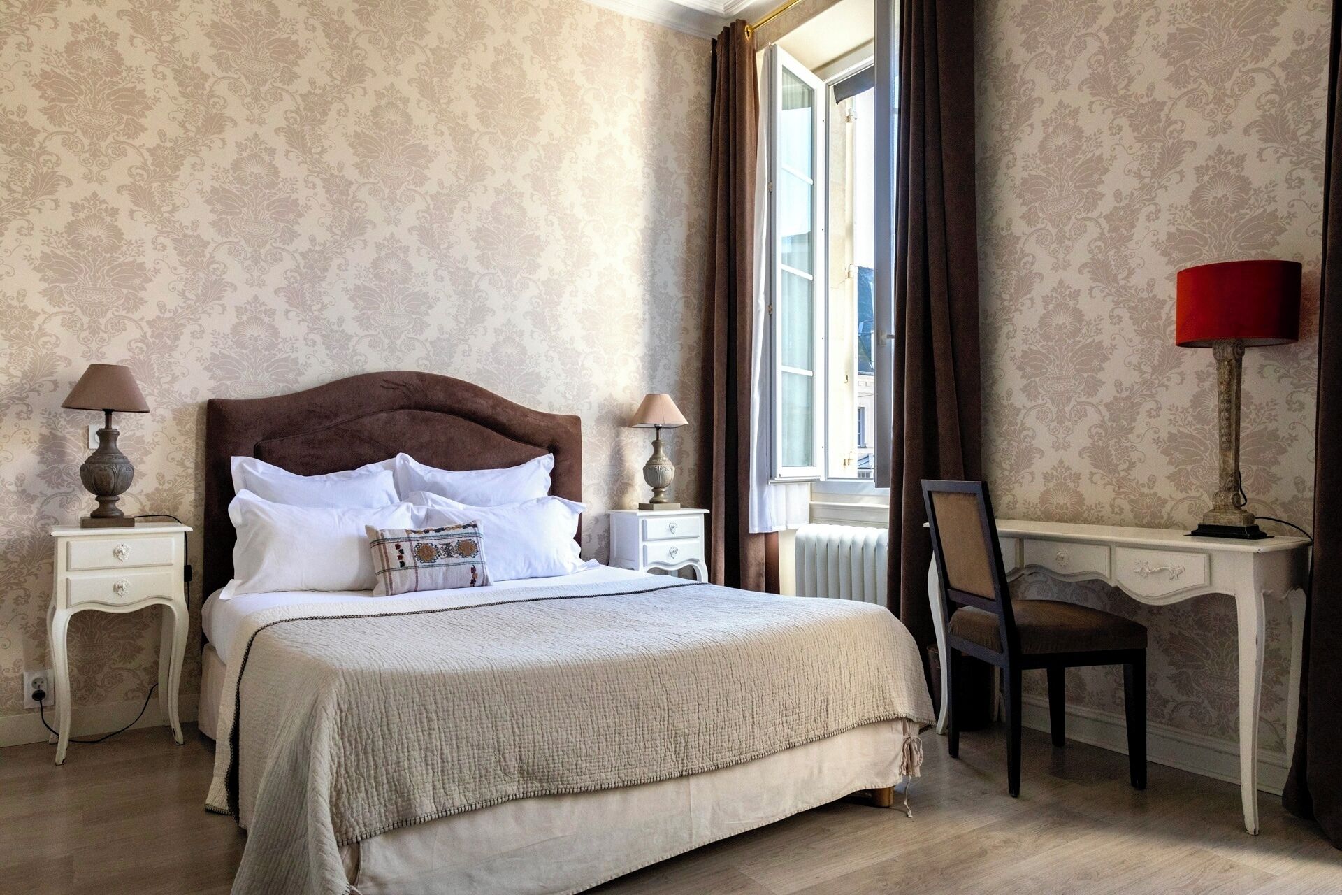 A neatly arranged bedroom with a large bed, two bedside tables with lamps, a chair, and a desk with a lamp.