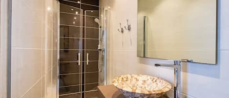 A modern bathroom with a glass-enclosed shower, a mosaic sink, and a large mirror.