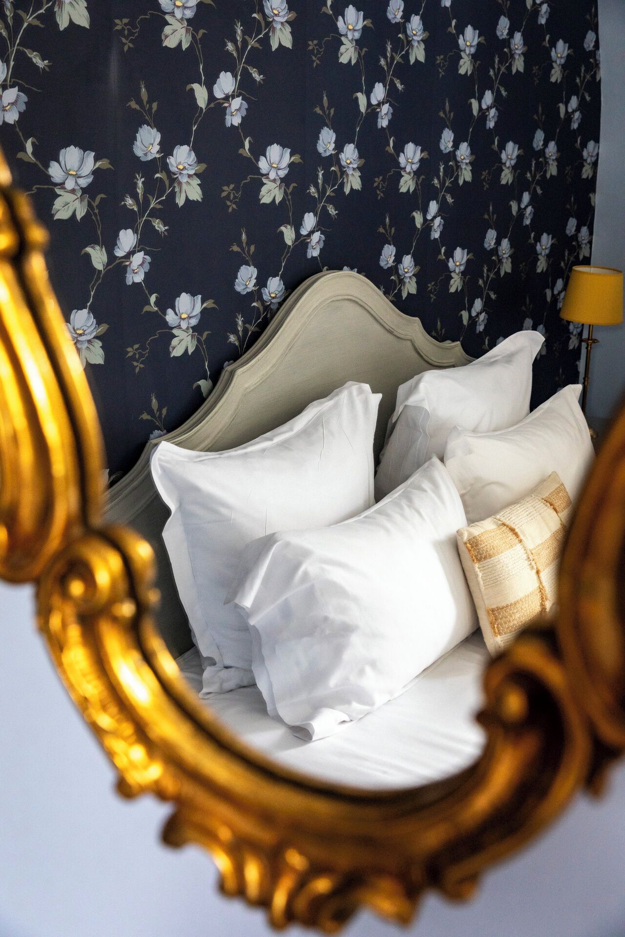 A bedroom with a bed, white pillows, a striped blanket, and a floral wallpaper.