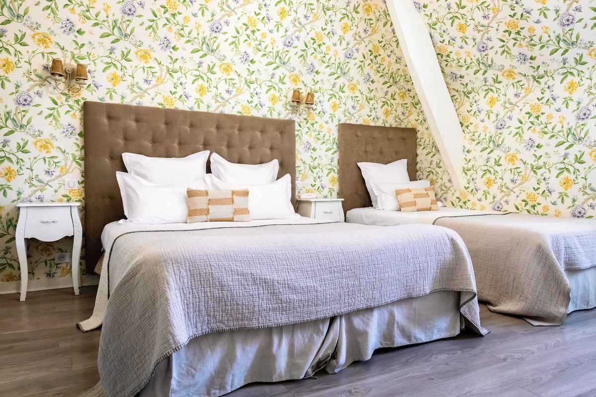 A double bed with a brown headboard, white bedding, and a floral wallpaper pattern.