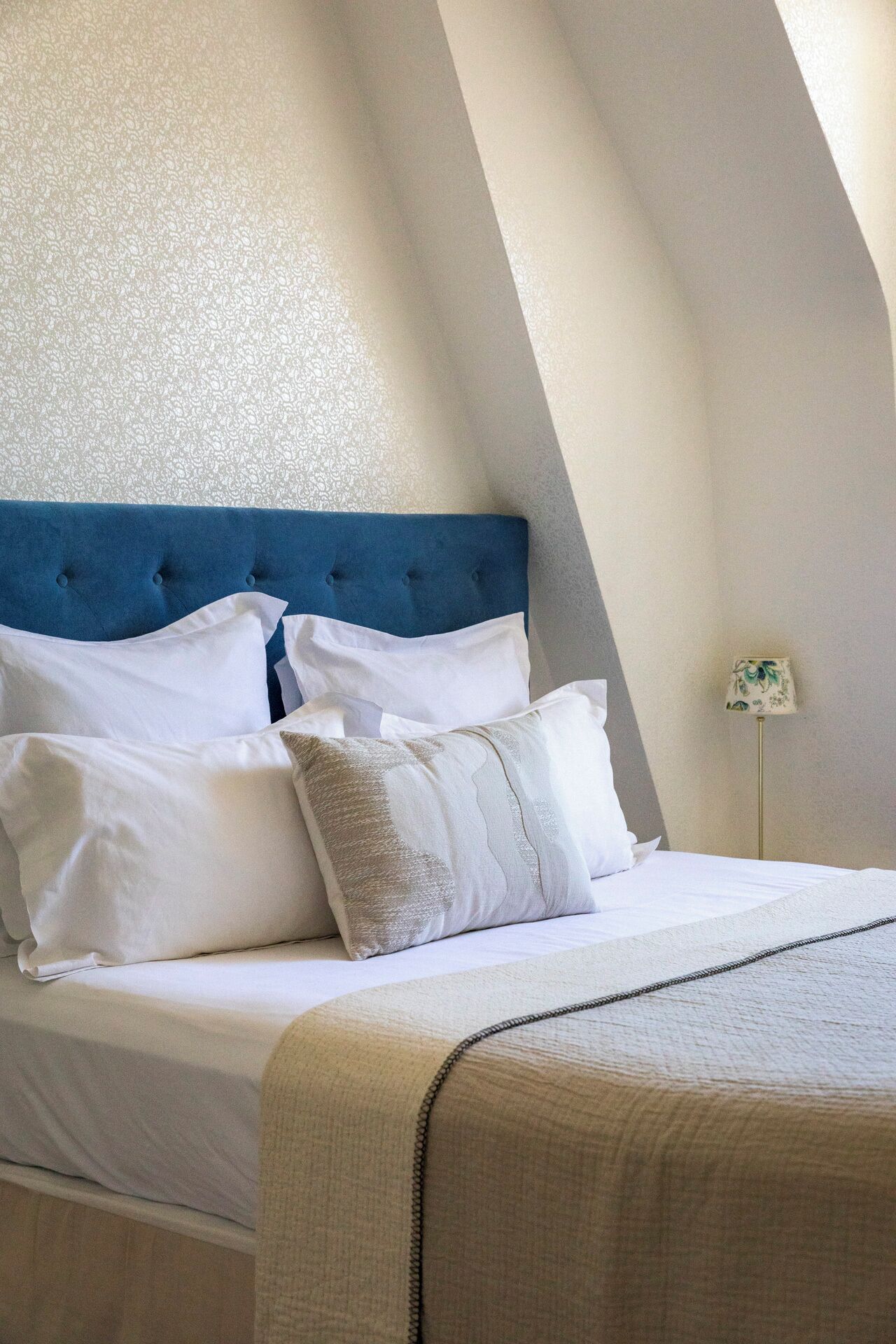 Une chambre à coucher avec une tête de lit bleue, du linge de lit blanc et une lampe sur un pied.