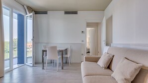 Ein modernes Wohnzimmer mit einer Couch, einem Esstisch mit Stühlen und einer Glastür, die auf einen Balkon im Freien führt.