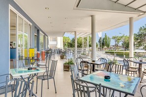 Un espace café extérieur avec des tables et des chaises, de grandes fenêtres et une vue sur la rue.