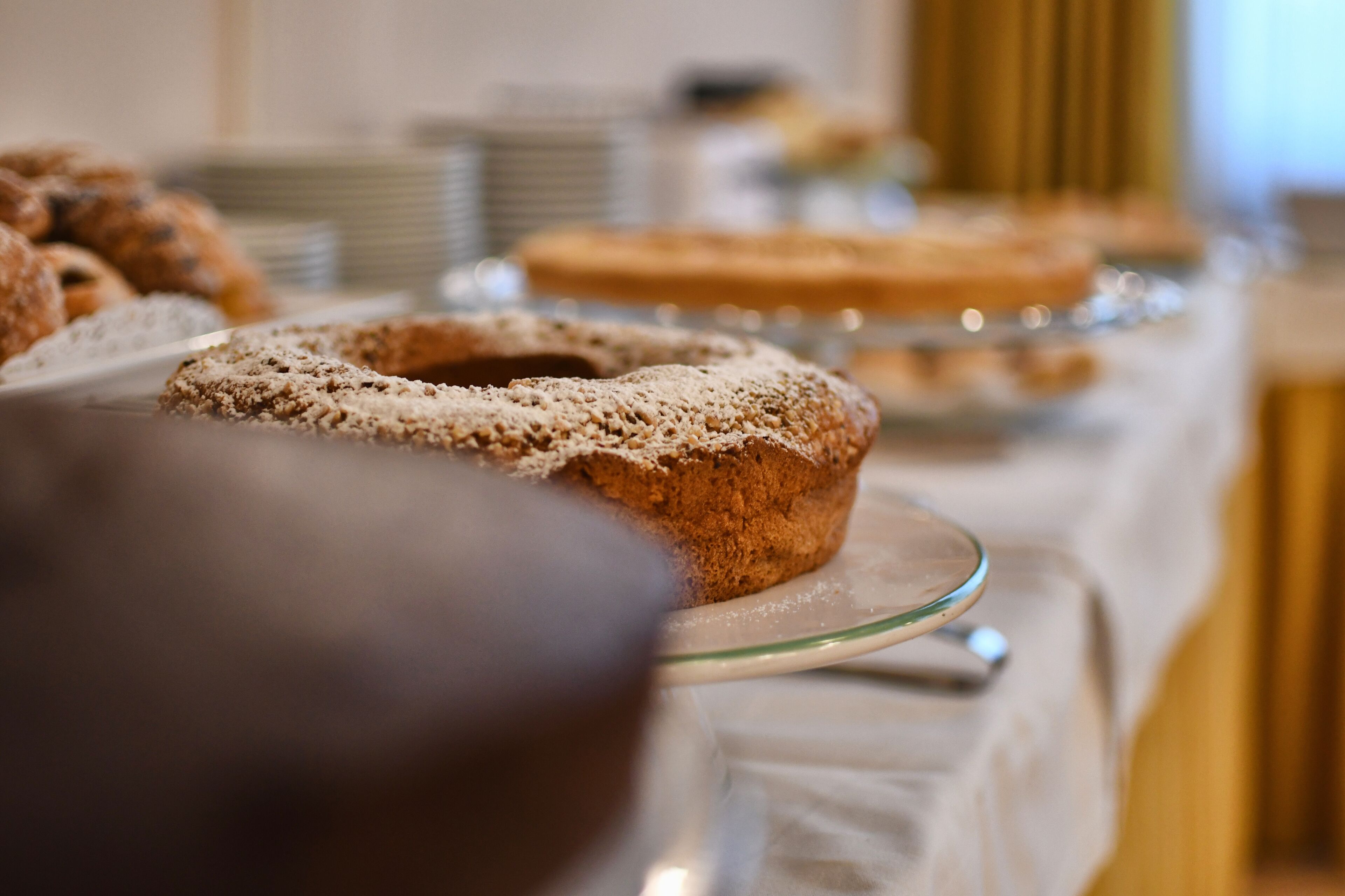 Una mesa de buffet con diversas opciones de repostería, incluyendo un pastel y bollería, cubierta con un mantel blanco.