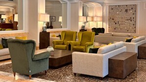 A spacious living room with a large chandelier, multiple seating options including a green armchair, a yellow armchair, and a grey sofa. - Hotel San Giorgio  Heaven Spa (Fiuggi)