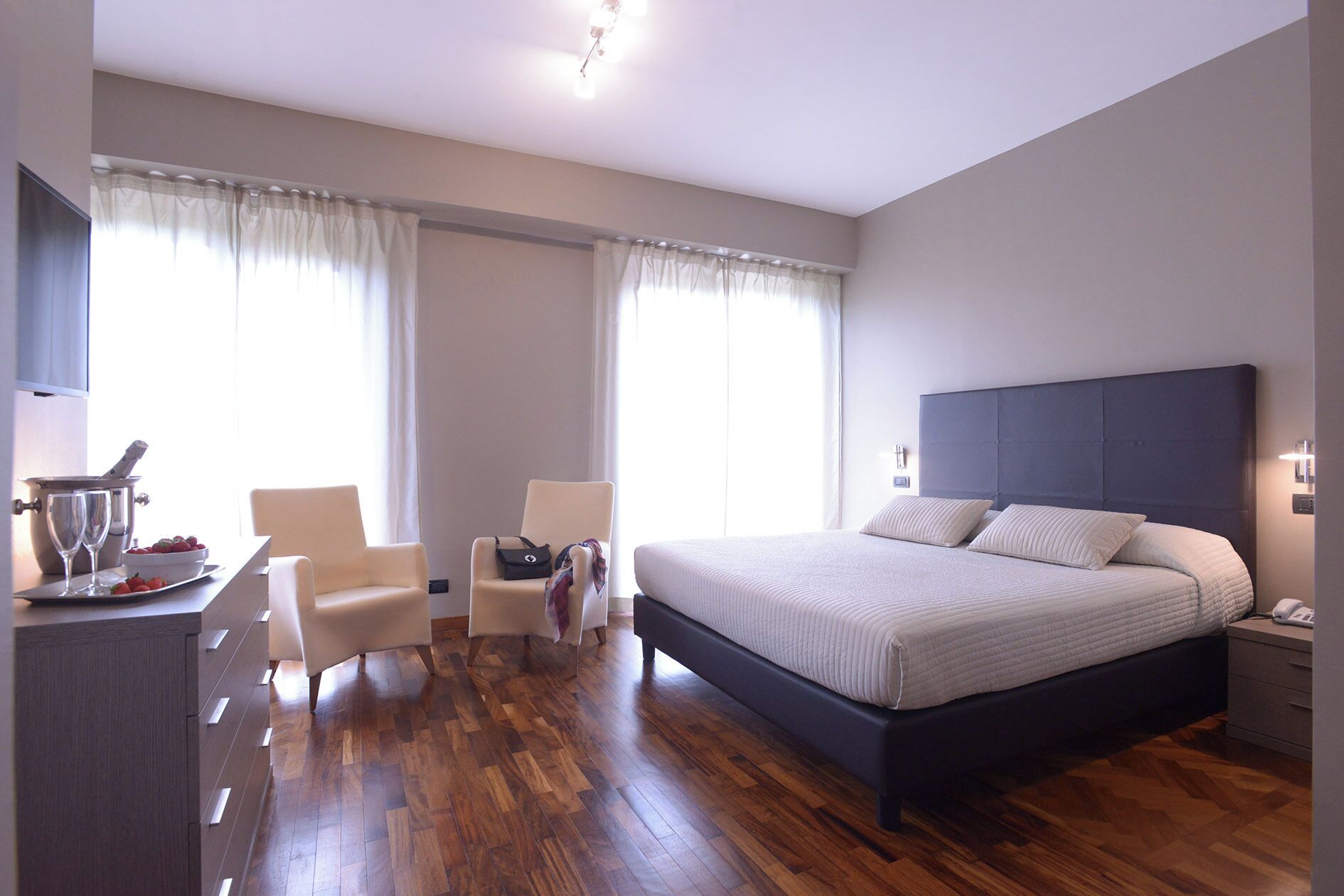 Een slaapkamer met een bed, nachtkastjes, een bureau met stoel, en een raam met gordijnen.