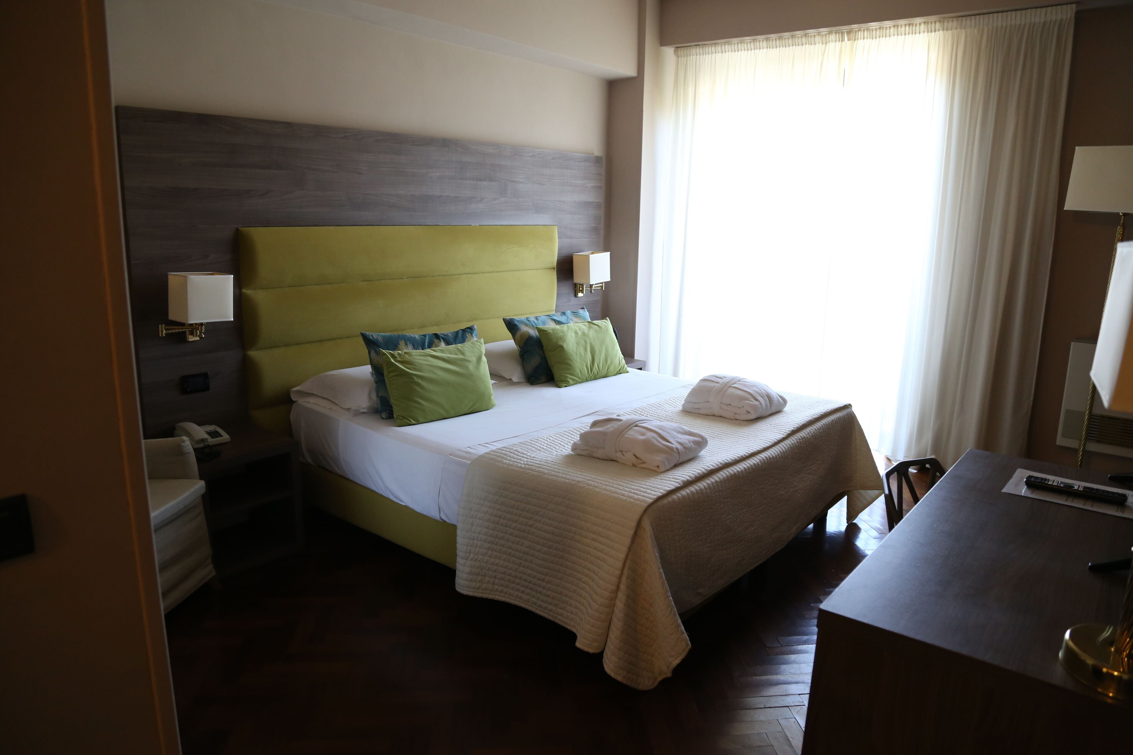A hotel room with a bed, bedside tables, a desk, and a window with curtains.