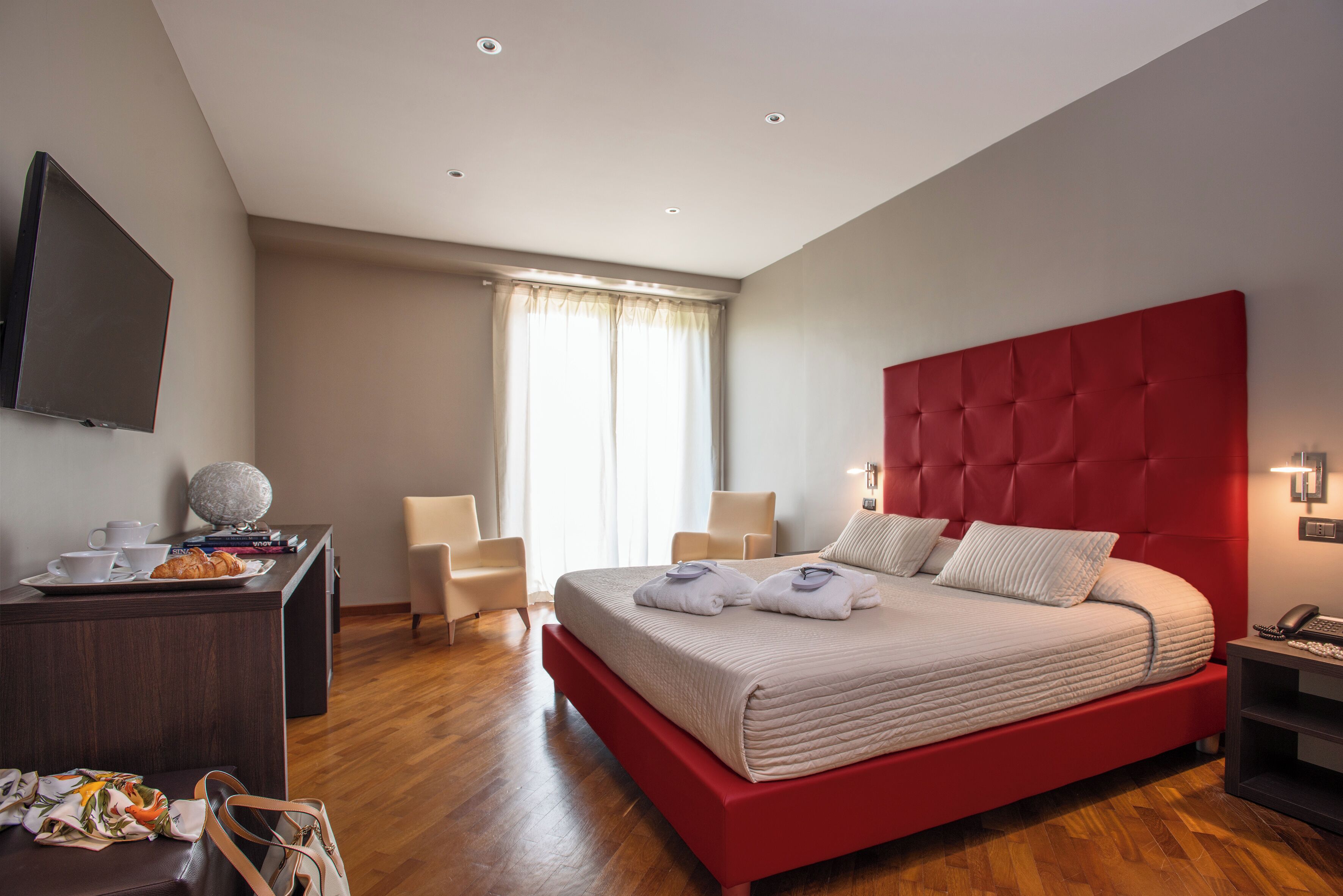 Un dormitorio moderno con una cama grande, un escritorio con televisión de pantalla plana, una silla y una ventana con cortinas.