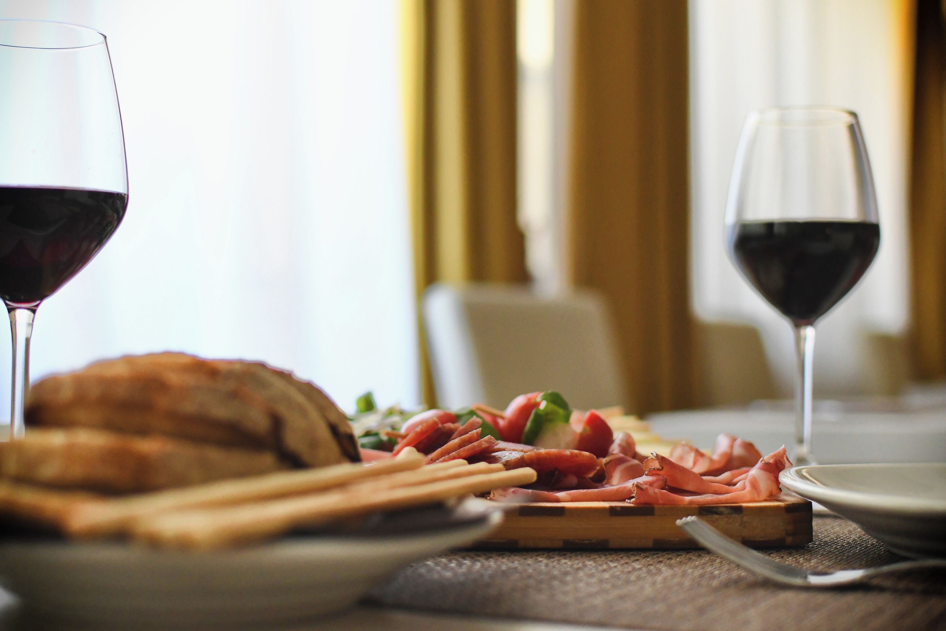 Una mesa de comedor con un plato de comida, dos copas de vino tinto y una hogaza de pan.