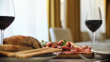 A dining table with a plate of food, two glasses of red wine, and a loaf of bread.