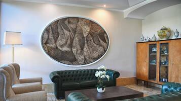 A living room with a large round wall art, a green sofa, a coffee table with a vase of flowers, a lamp, and a cabinet with decorative items.