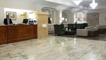 Un hall d’hôtel comprenant un comptoir d’accueil, un espace salon et des lustres.