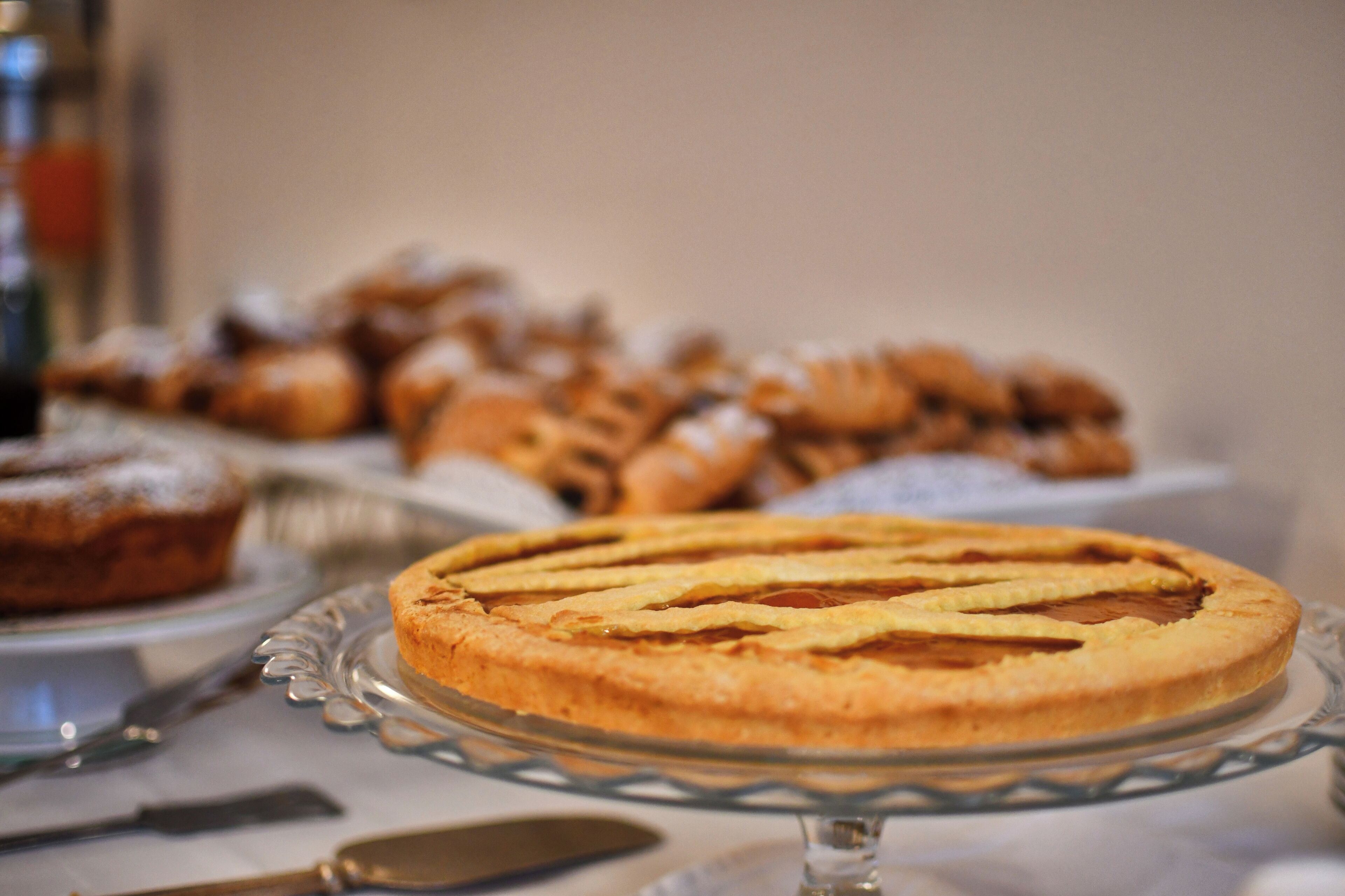 A pie on a glass stand with a blurred background of pastries.