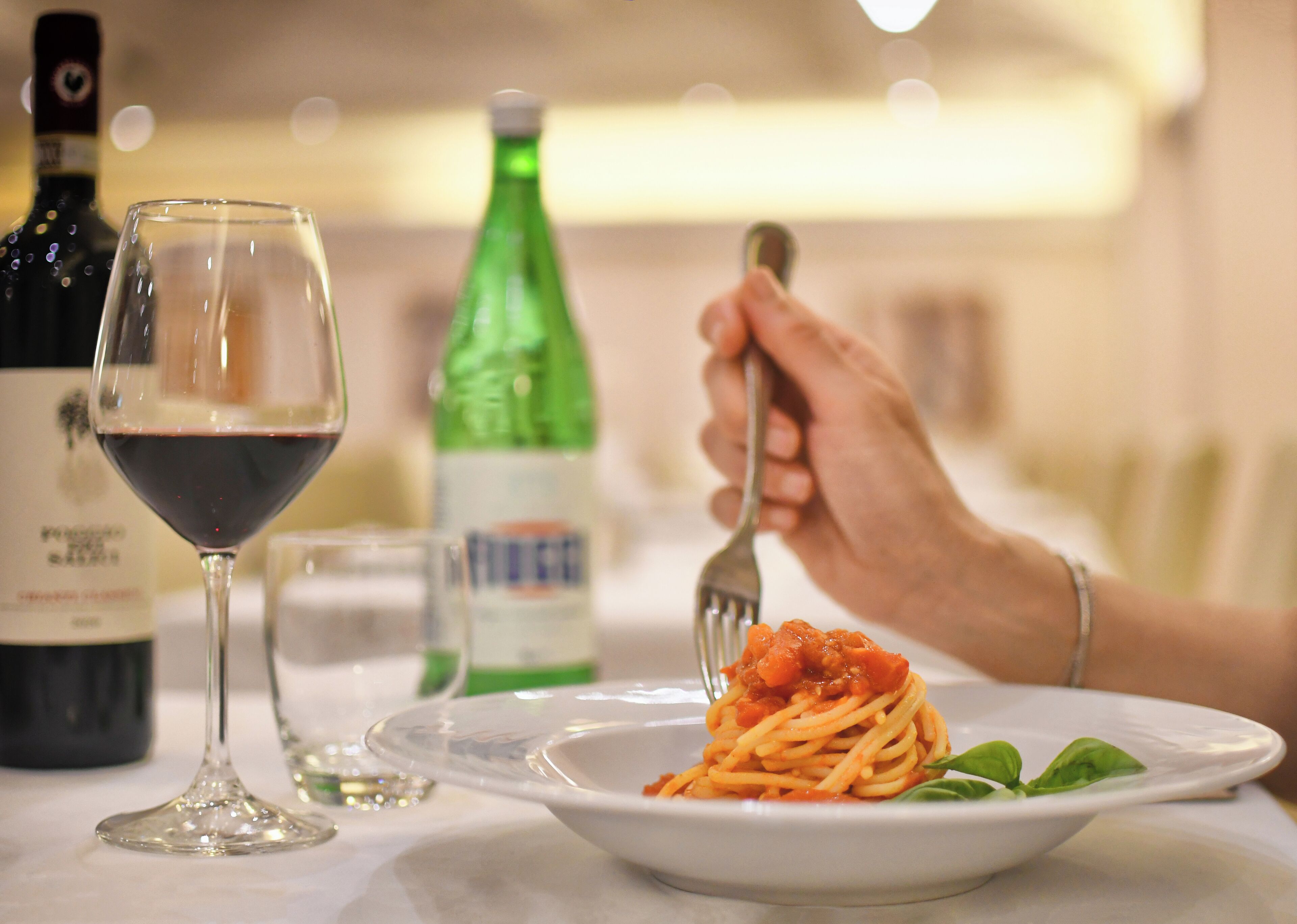 Une table à manger avec une assiette de spaghettis, un verre de vin rouge et une bouteille verte.