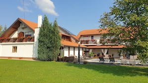 A traditional European-style building with a red-tiled roof, a large coniferous tree, and outdoor seating area. - House Tina - Bed and Breakfast (Rakovica)