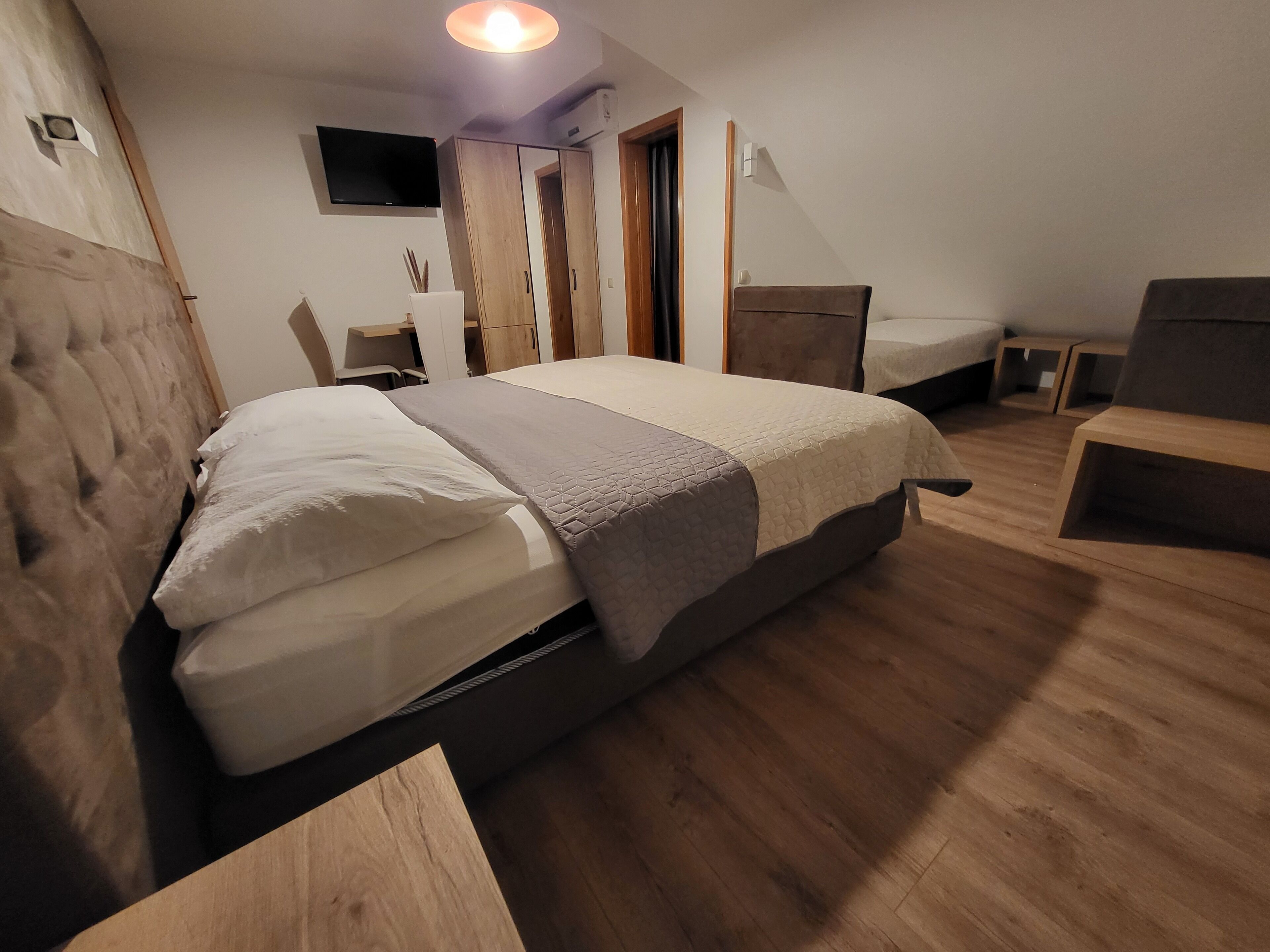 A bedroom with a bed, a desk, a chair, and a TV on the wall.
