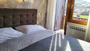 A bedroom with a large bed, a radiator, and a view of a rural landscape through a window. - House Tina - Bed and Breakfast (Rakovica)