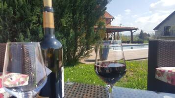 Una botella de vino y una copa de vino tinto sobre una mesa al aire libre, con vista a una piscina y una casa al fondo.