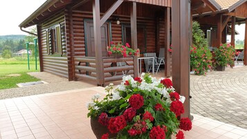Una cabaña de madera con porche, mobiliario exterior y jardineras con flores.