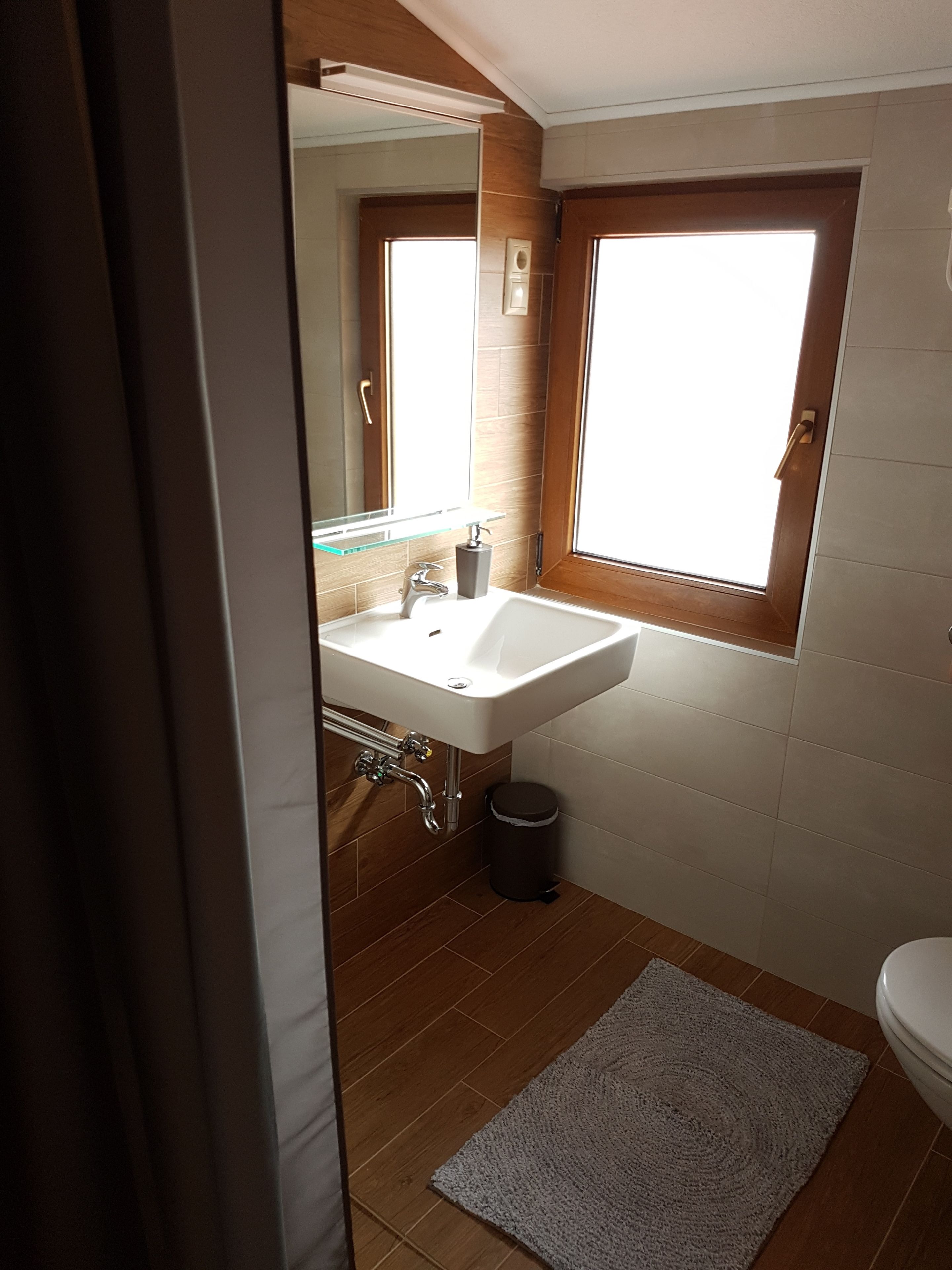 A bathroom with a white sink, a window, a mirror, and a toilet.