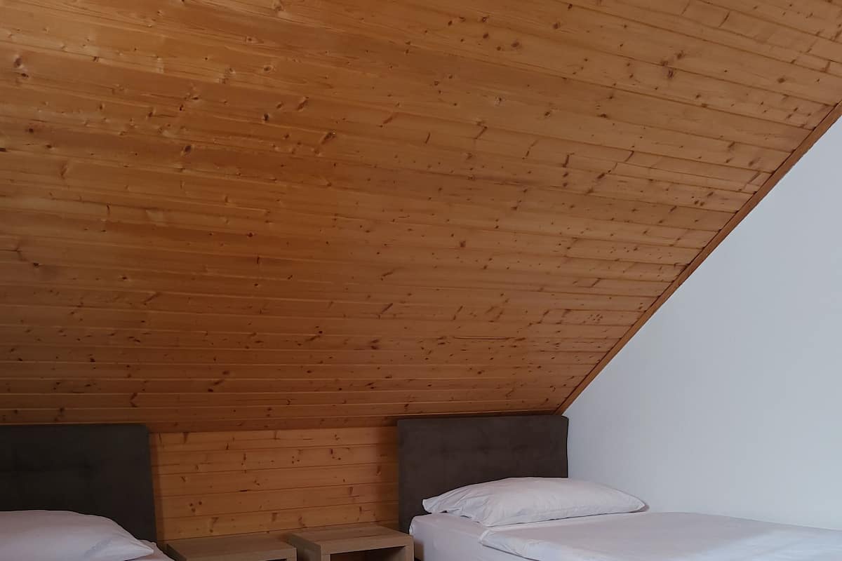 A small, cozy room with two beds, wooden flooring, and a sloped ceiling.