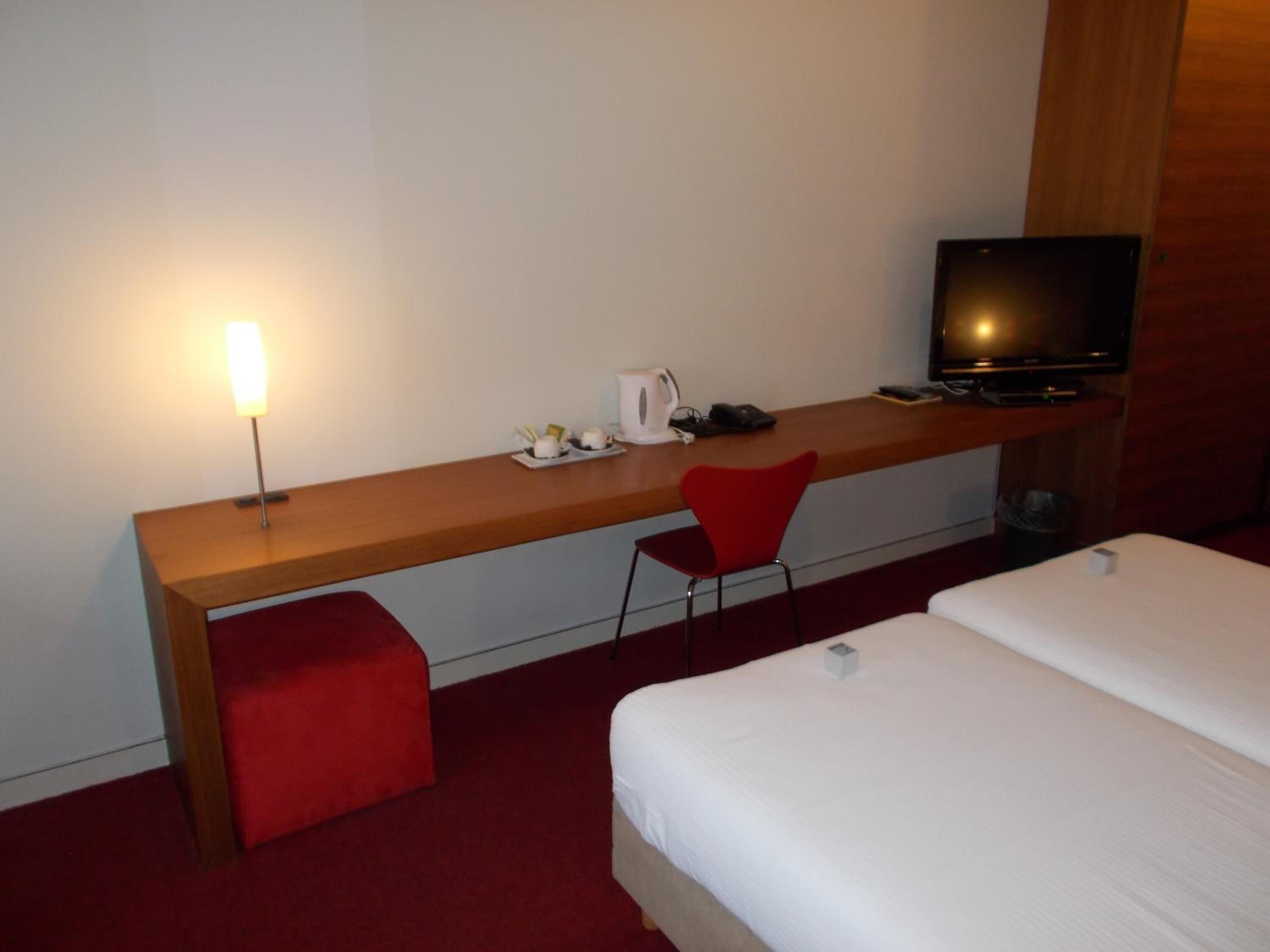 A hotel room with a wooden desk, a red chair, a television, and two beds.